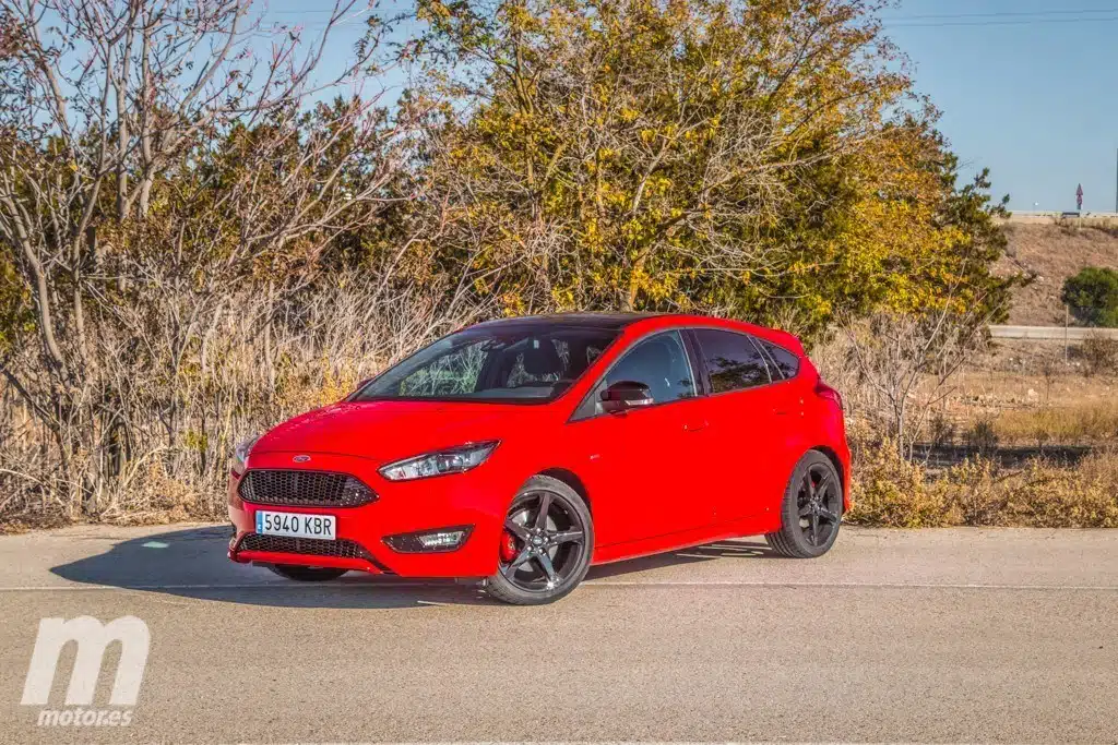 Los 12 mejores coches de segunda mano por menos de 10.000 euros 3 Ford Focus 20 TDCi de color rojo estacionado en la carretera, de fondo se ven árboles verdes y amarillos.
