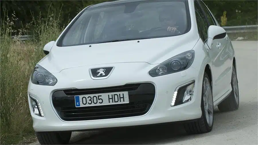 Los 12 mejores coches de segunda mano por menos de 10.000 euros 4 Peugeot 308 2.0 HDI de color blanco conducido por un hombre doblando una curva pronunciada.