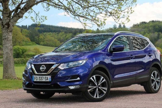 Los 16 mejores coches de segunda mano para comprar en 2026 9 Nissan Qashqai azul aparcado en un camino rural con árboles y campos verdes al fondo