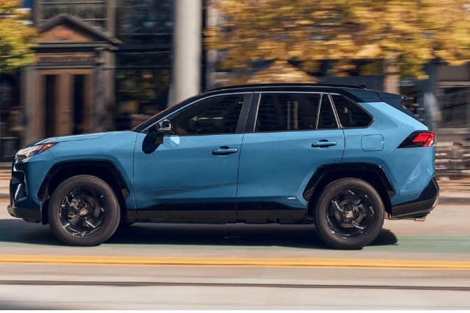 Los 16 mejores coches de segunda mano para comprar en 2026 11 Toyota RAV4 Hybrid azul con techo negro circulando por una calle urbana en otoño