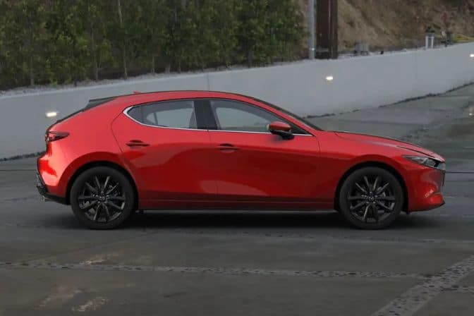 Los 16 mejores coches de segunda mano para comprar en 2026 8 Mazda 3 rojo de cinco puertas visto de perfil aparcado sobre asfalto húmedo