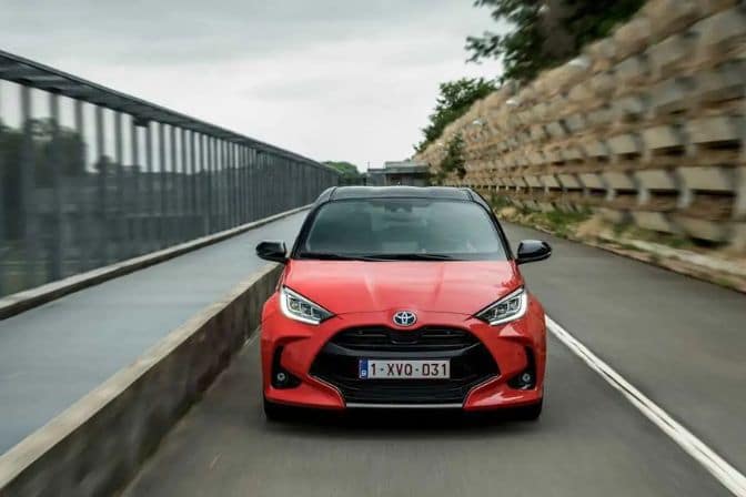 Los 16 mejores coches de segunda mano para comprar en 2026 3 Toyota Yaris Híbrido rojo circulando por carretera entre barrera metálica y vegetación