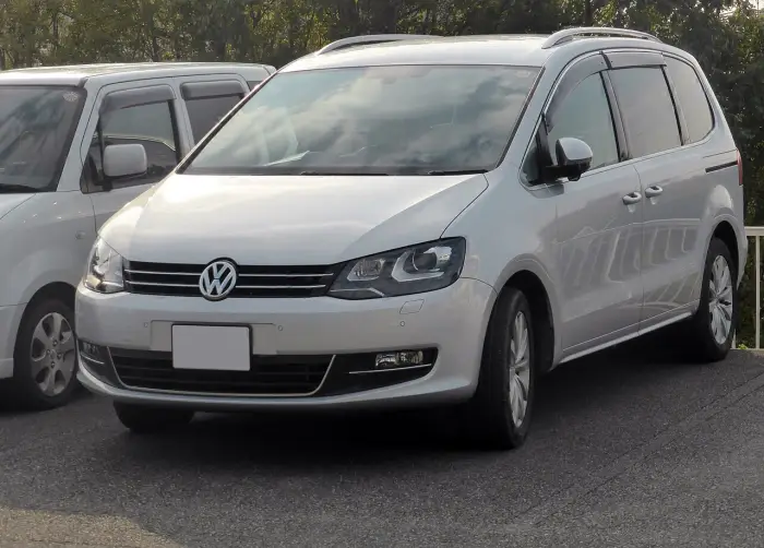 Los 24 mejores coches familiares de 7 plazas de ocasión 2 Volkswagen Sharan II plateado aparcado junto a una furgoneta blanca, de tres cuartos delantero y con árboles detrás