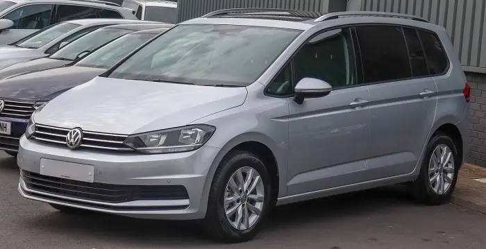 Los 24 mejores coches familiares de 7 plazas de ocasión 3 Volkswagen Touran Mk2 gris plata aparcado en una fila de coches de un concesionario, de tres cuartos delantero
