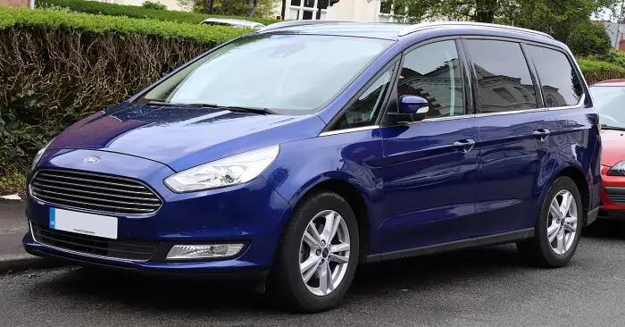 Los 24 mejores coches familiares de 7 plazas de ocasión 4 Ford Galaxy Mk3 azul oscuro aparcado junto al bordillo ante un seto y una casa, visto de tres cuartos delantero