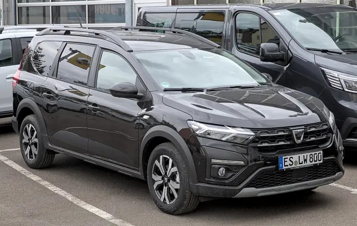 Los 24 mejores coches familiares de 7 plazas de ocasión 7 Dacia Jogger negro con barras de techo y matrícula alemana, aparcado de tres cuartos delantero entre otros coches