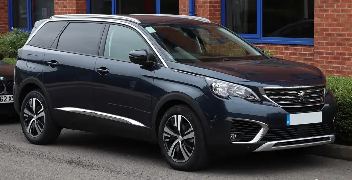Los 24 mejores coches familiares de 7 plazas de ocasión 9 Peugeot 5008 II azul oscuro aparcado junto al bordillo, de tres cuartos delantero ante un edificio de ladrillo