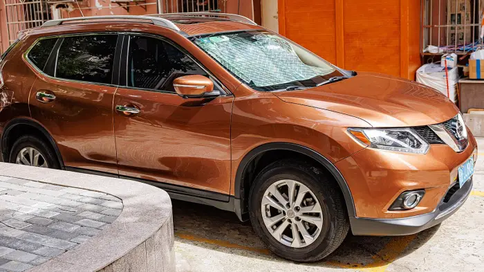 Los 24 mejores coches familiares de 7 plazas de ocasión 12 Nissan X-Trail T32 naranja cobre aparcado en una calle estrecha, de tres cuartos delantero y con parasol al sol