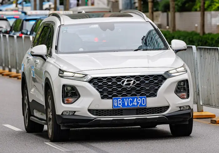 Los 24 mejores coches familiares de 7 plazas de ocasión 13 Hyundai Santa Fe TM blanco circulando de frente por una avenida urbana, con una valla metálica y arbolado al fondo