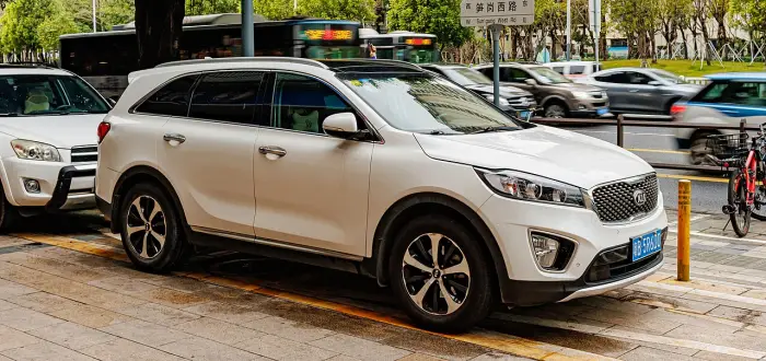 Los 24 mejores coches familiares de 7 plazas de ocasión 14 Kia Sorento UM blanco aparcado sobre la acera de una avenida, de tres cuartos delantero con autobuses al fondo