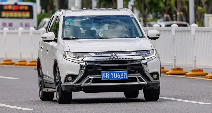 Los 24 mejores coches familiares de 7 plazas de ocasión 16 Mitsubishi Outlander blanco circulando de frente, con el nombre del modelo en el capó y una valla blanca al fondo