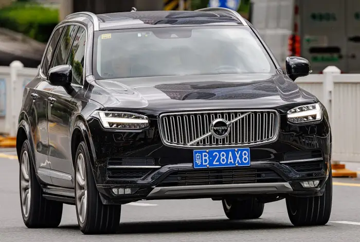 Los 24 mejores coches familiares de 7 plazas de ocasión 17 Volvo XC90 II negro circulando de frente por una avenida urbana, con la parrilla cromada y una valla blanca detrás