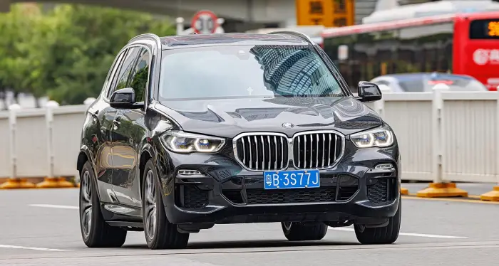 Los 24 mejores coches familiares de 7 plazas de ocasión 19 BMW X5 G05 negro circulando de frente por una avenida, con una señal de límite 30 y un autobús rojo desenfocados