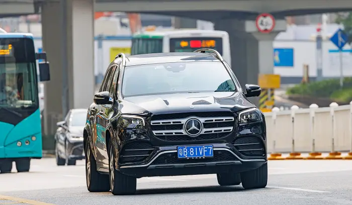 Los 24 mejores coches familiares de 7 plazas de ocasión 22 Mercedes GLS X167 negro circulando de frente por una avenida, con autobuses y señales de tráfico desenfocados detrás