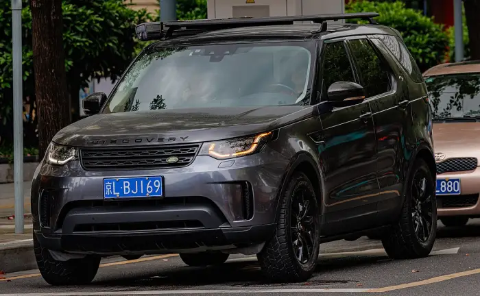 Los 24 mejores coches familiares de 7 plazas de ocasión 23 Land Rover Discovery 5 gris oscuro con bandeja portaequipajes en el techo, aparcado junto al bordillo entre árboles