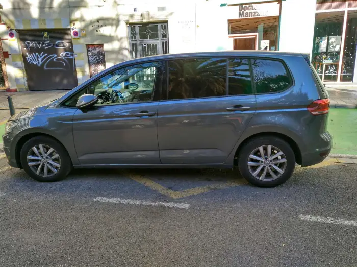 Los 21 mejores monovolúmenes de segunda mano para 2026 10 Volkswagen Touran gris de perfil, aparcado en una calle con comercios y marcas de zona verde